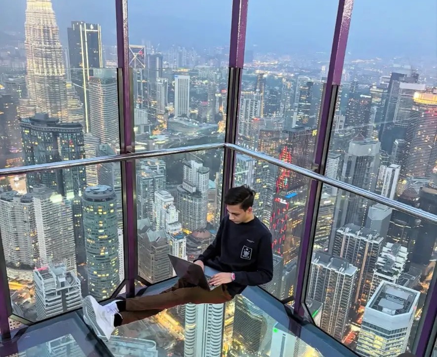 Furqan Sheikh working on a laptop above the Kuala Lumpur skyline